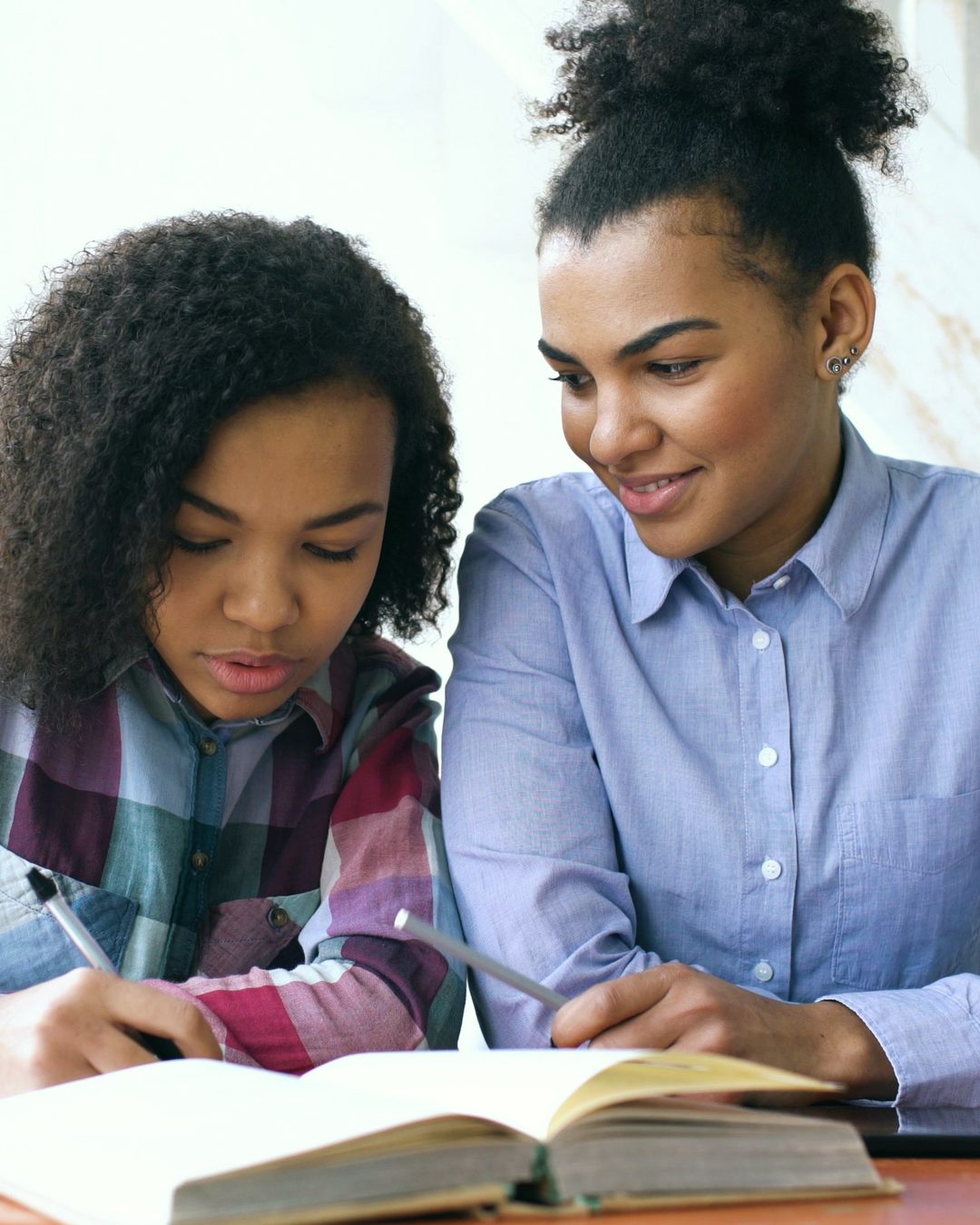 Tutor smiling as a teenage student writes notes beside an open textbook at a table
