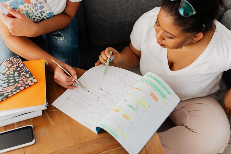 Overhead view of a tutor and student going through highlighted revision notes in an exercise book